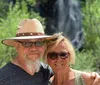 A smiling couple poses in front of a waterfall surrounded by green foliage