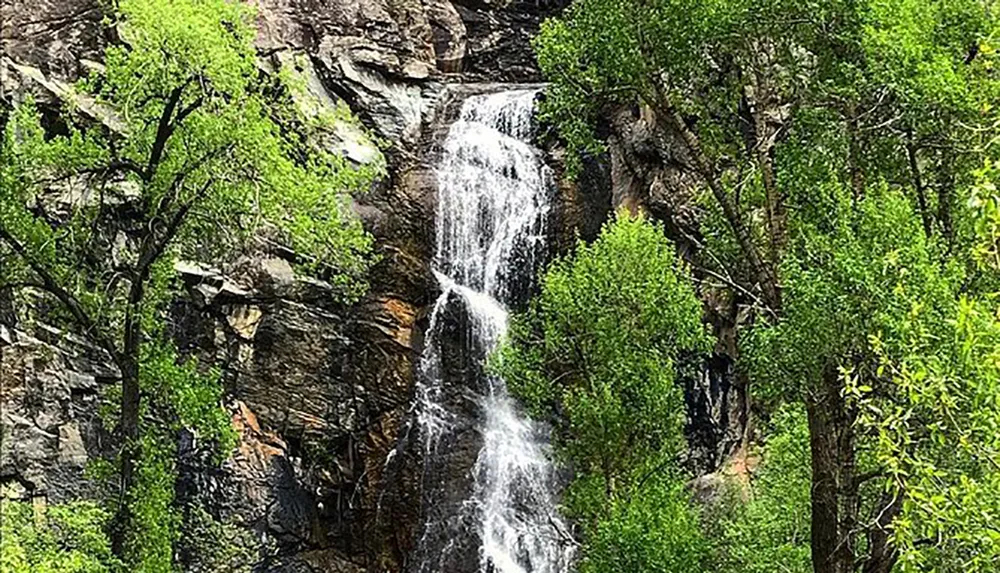 The image shows a serene waterfall cascading down a rocky cliff amidst lush green foliage