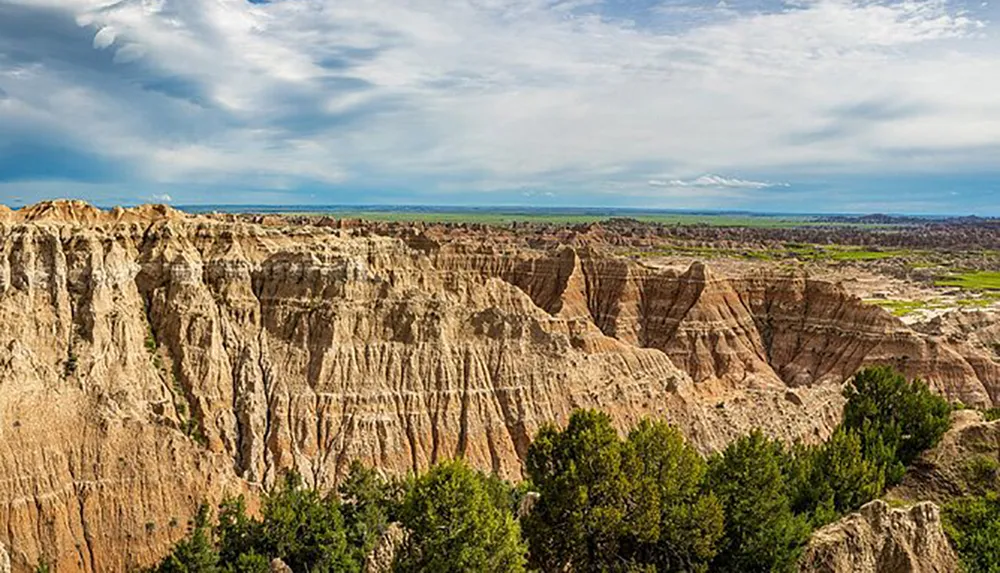 The image shows a panoramic view of the rugged striated landscape of Badlands National Park under a vast sky with scattered clouds