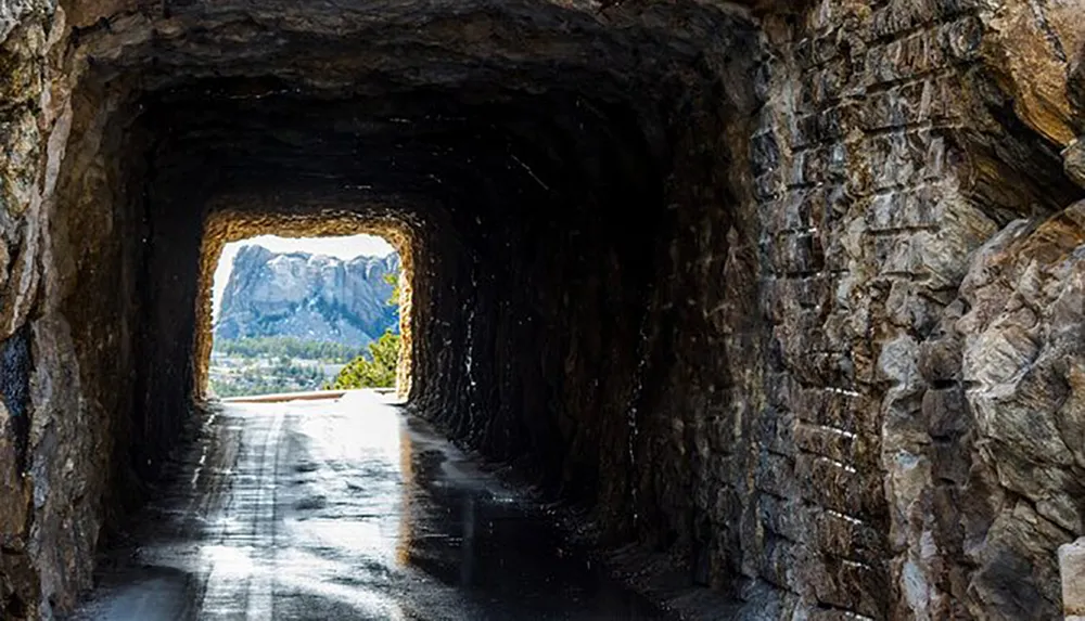 This image shows a view through a dark rocky tunnel opening up to a bright landscape with a mountain in the distance