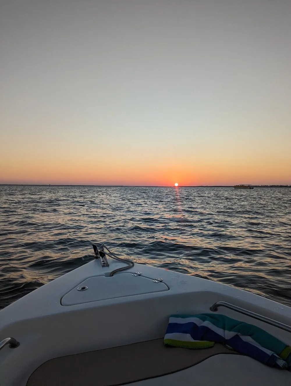 A serene view of a sunset from the bow of a boat floating on calm waters