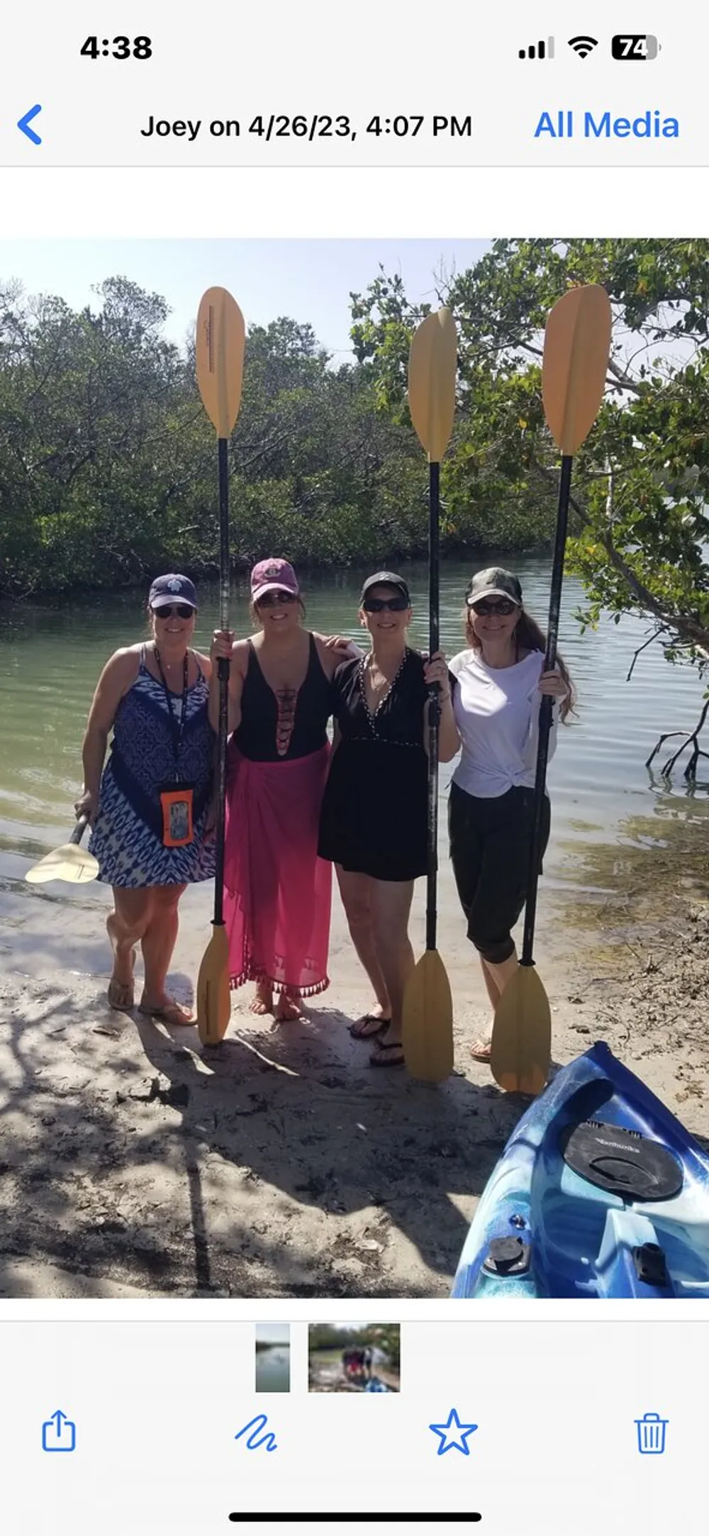 Four people are standing on a beach holding kayak paddles with mangroves in the background