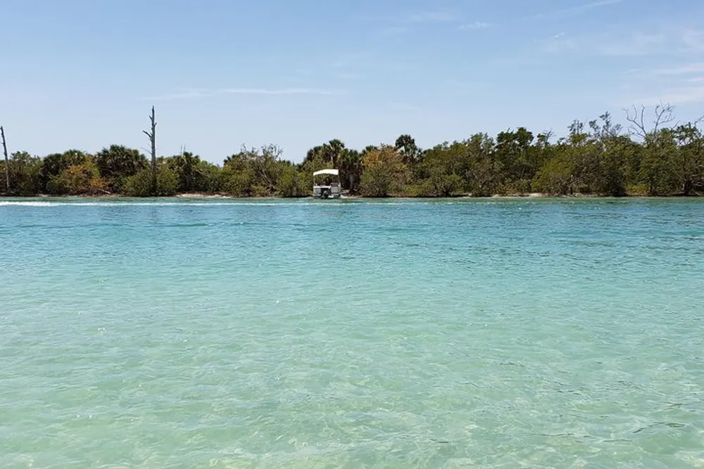 The image shows a serene tropical scene with clear turquoise waters in the foreground and a lush green island with a small white building in the distance under a blue sky