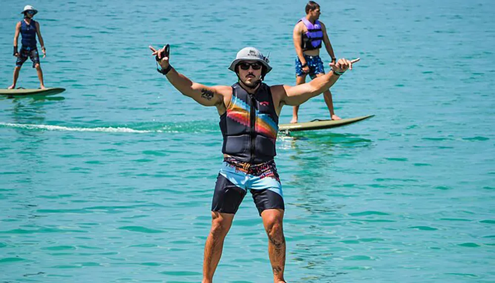 A person is striking a playful pose on a paddleboard in the water while two other individuals stand on paddleboards in the background