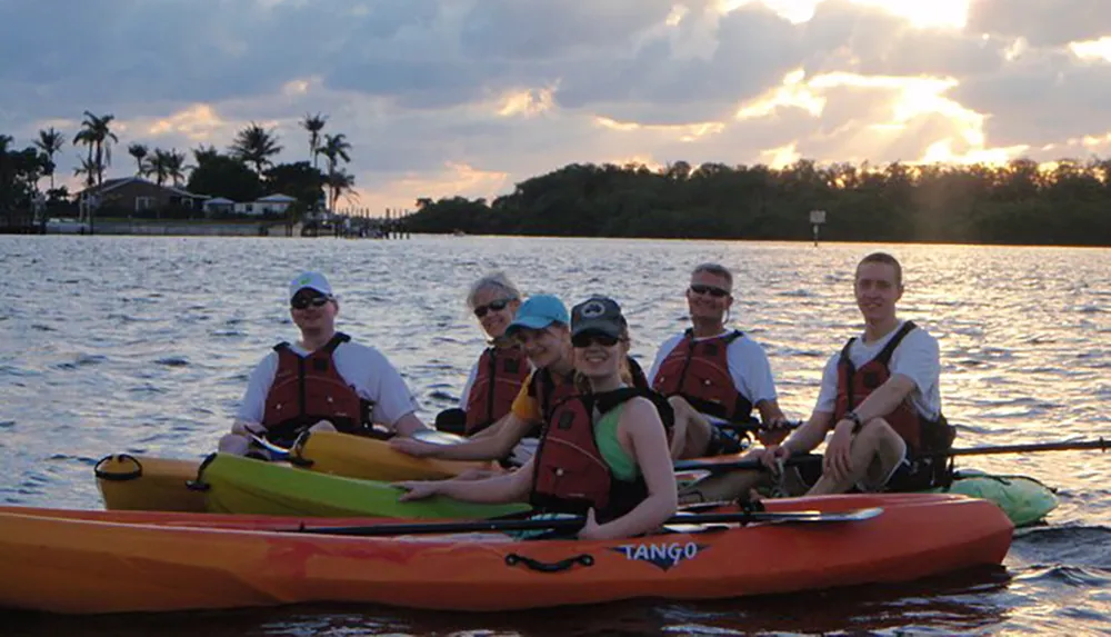 A group of people in life jackets are enjoying a kayaking adventure on a body of water with a backdrop of a beautiful sunset and coastal scenery