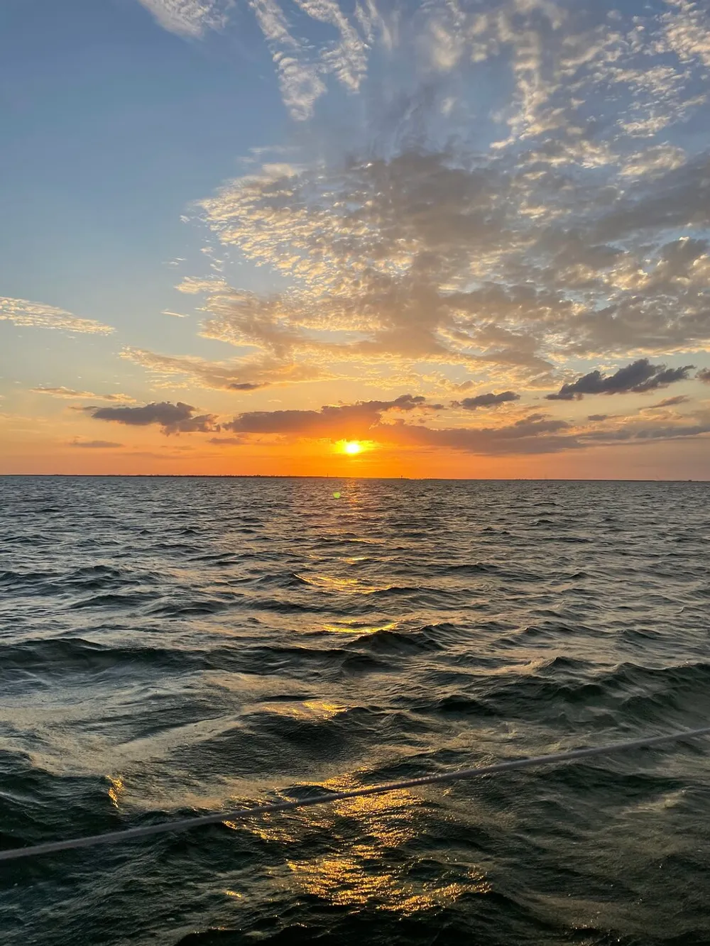 The image captures a serene sunset over choppy ocean waters with luminous clouds scattered across the sky