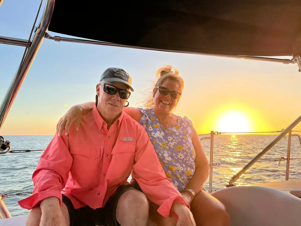 A man and a woman are posing with smiles on a boat during a sunset over the ocean