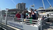 A group of people is posing for a photo on a sunny day on the deck of a boat named 