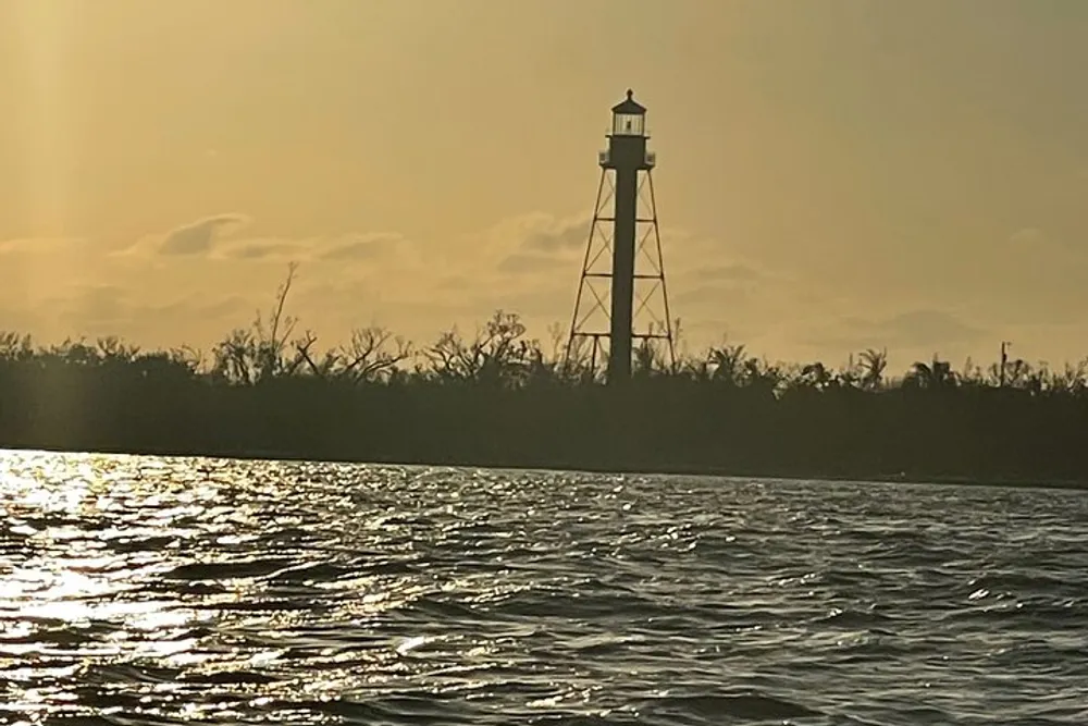 The image shows a silhouette of a lighthouse against a golden sunset reflected in the waters surface