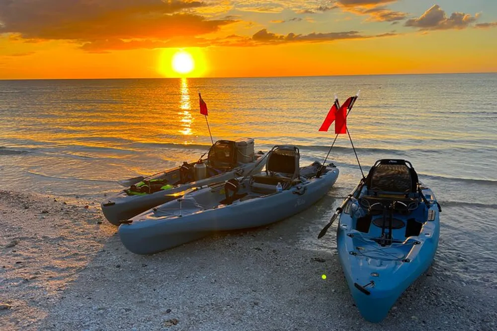 Two kayaks rest on a sandy beach as the sun sets over a calm sea