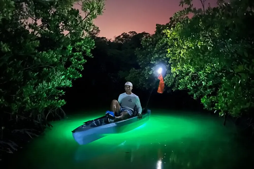 A person is night kayaking with underwater lights illuminating the water in a vibrant green as a dusk sky fades in the background