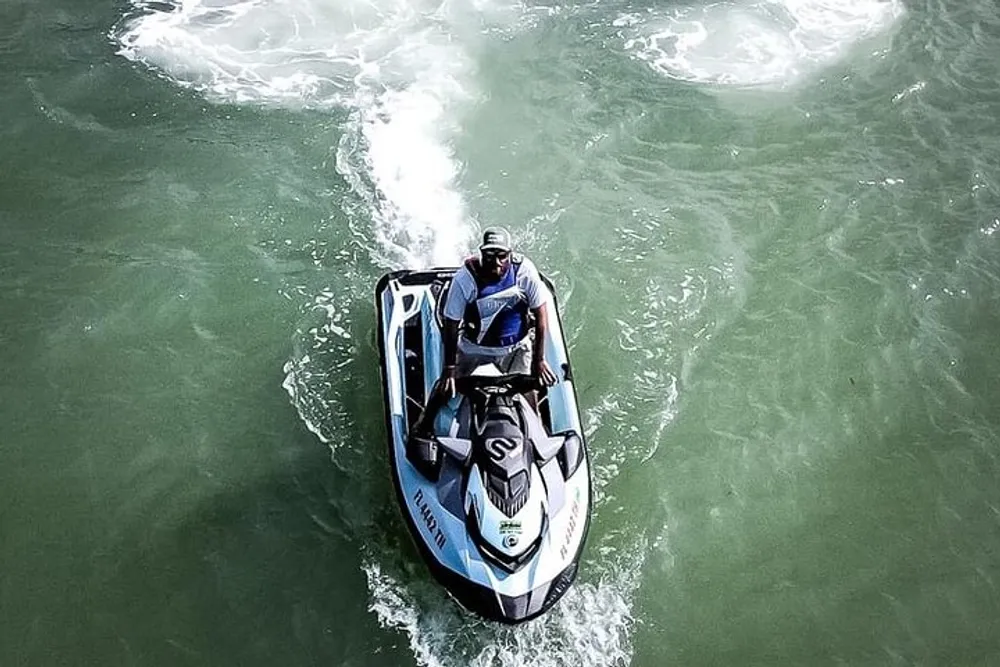 A person is riding a jet ski on greenish waters creating a frothy wake behind them