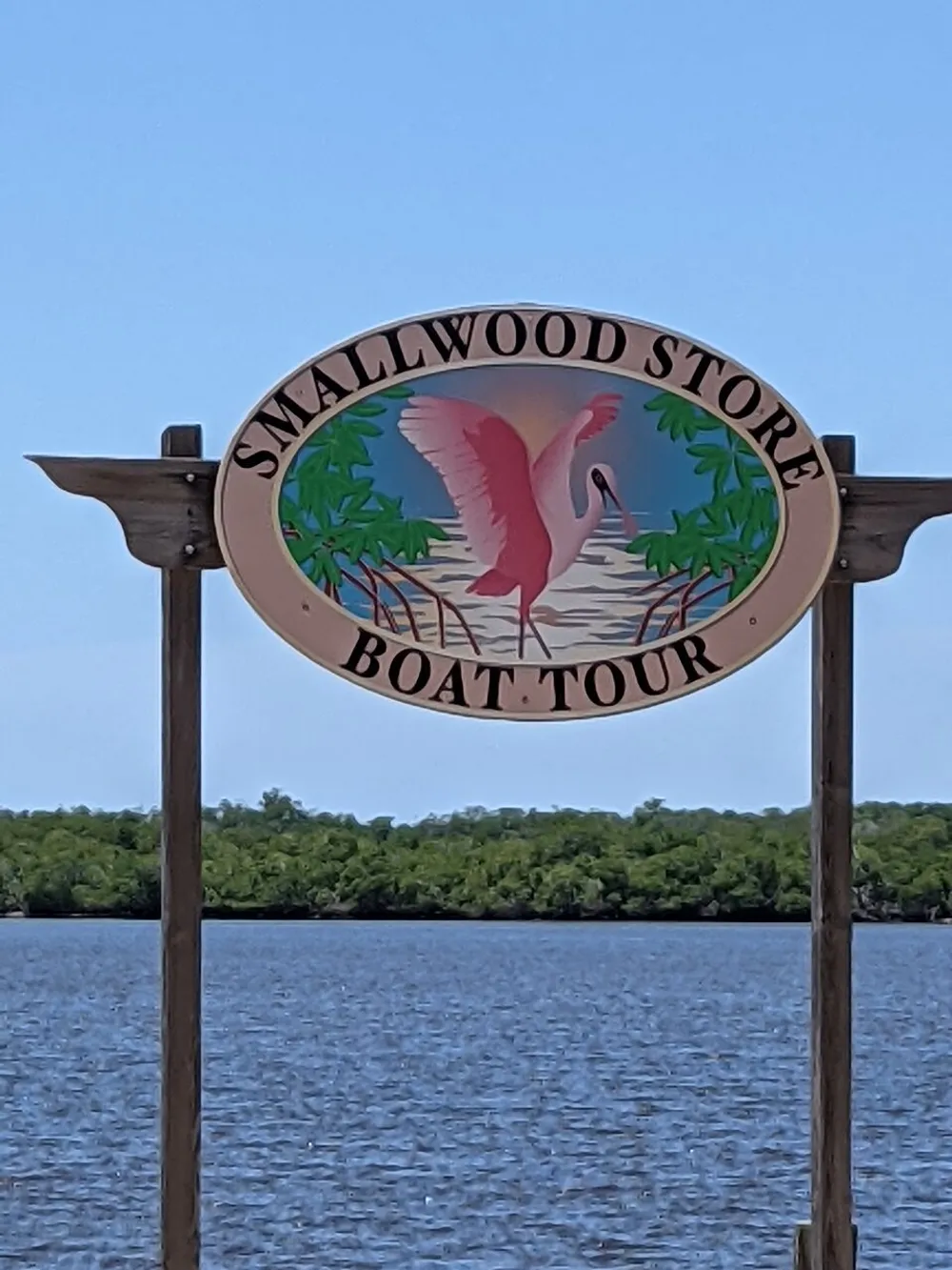 The image shows an oval-shaped sign with the text SMALLWOOD STORE BOAT TOUR and an illustration of a pink flamingo set against a backdrop of water and greenery