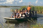 A group of people is enjoying an airboat tour through a marshy waterway.