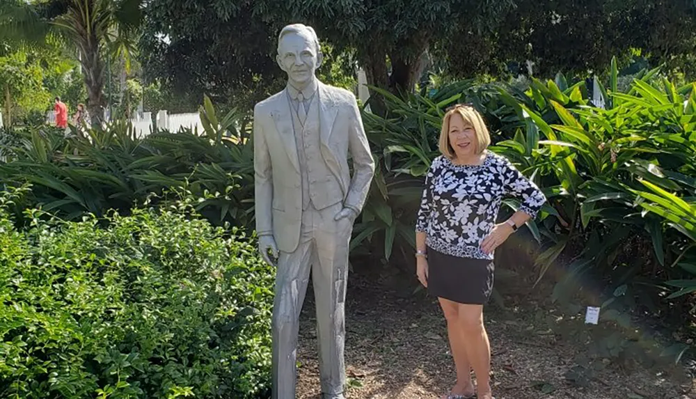 A person is standing next to a statue of a man in a garden setting smiling at the camera