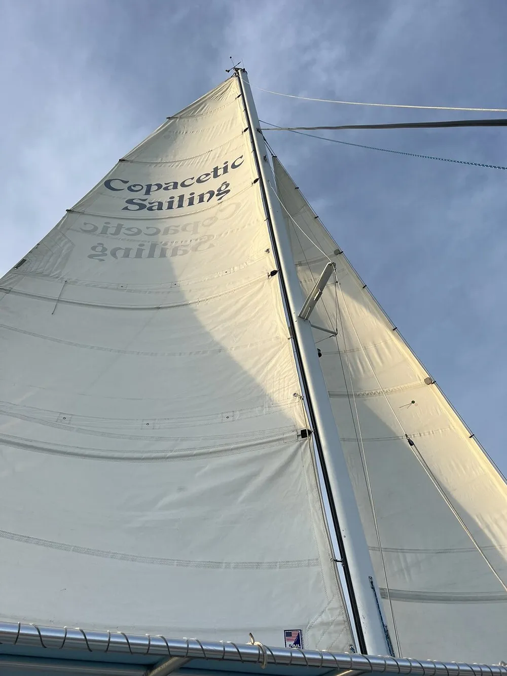 The image showcases the mainsail of a sailboat hoisted up the mast featuring the text Copacetic Sailing against a blue sky