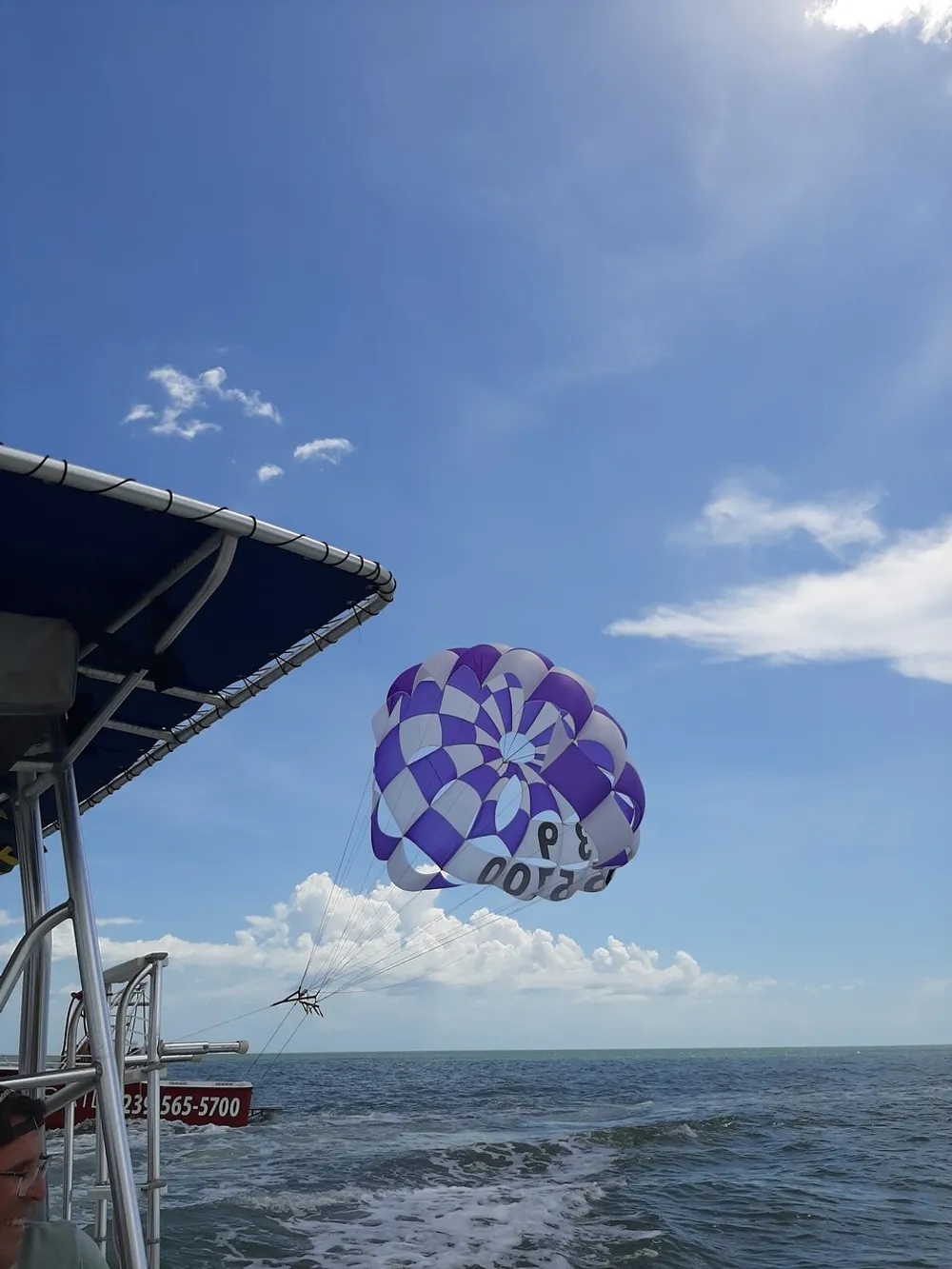A person is parasailing over the ocean on a sunny day tethered to a boat with a colorful parachute