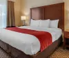 This image shows a neatly made bed with white linens and a red throw in a clean and simple hotel room