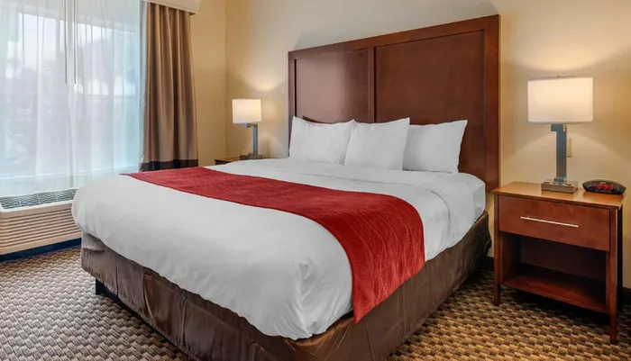 This image shows a neatly made bed with white linens and a red throw in a clean and simple hotel room