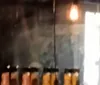 The image is blurry but it appears to show a row of items that could be candles or glasses on a table with a hanging light fixture on the left and a bright light source like a door or window on the right