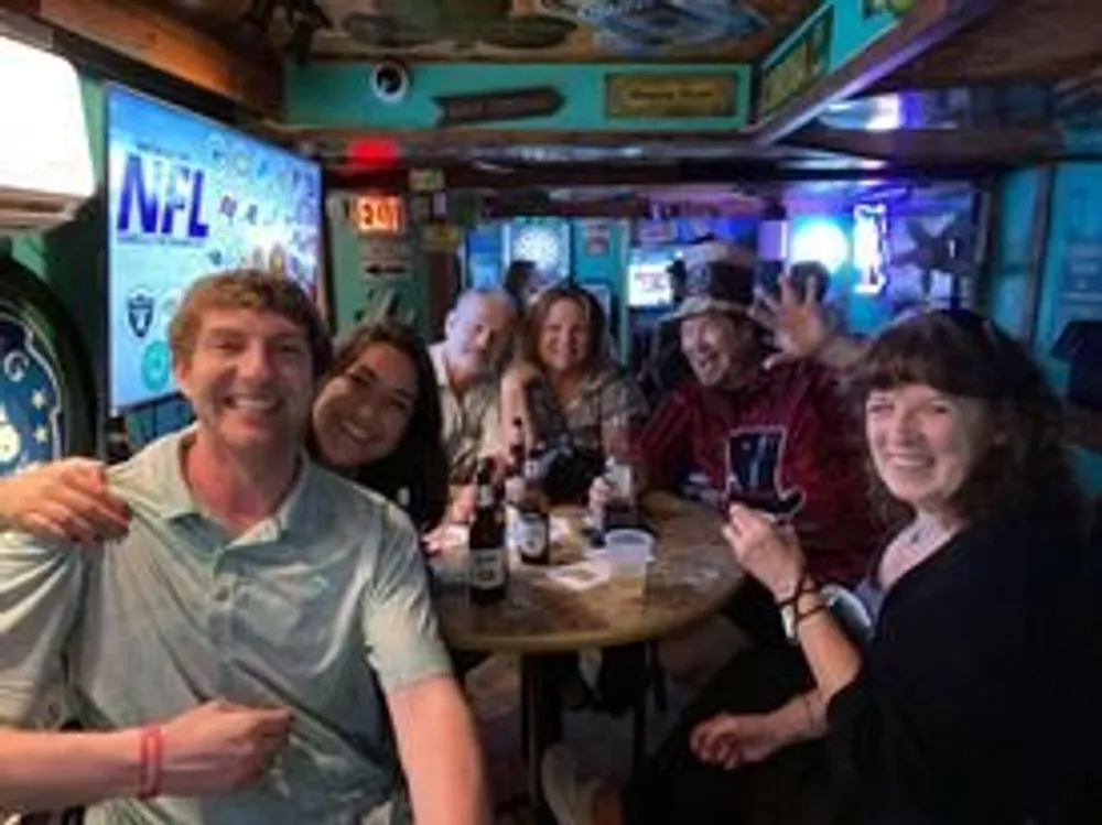 A group of cheerful people are posing for a photo in a lively bar with sports memorabilia on the walls
