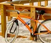 An orange bicycle is casually leaned against a wooden railing on a sandy beach under bright sunlight