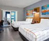 The image shows a modern and neatly arranged hotel room with twin beds colorful wall art and a separate space visible through sliding doors