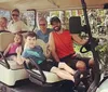 A group of people including adults and children are smiling and posing for a photo in a golf cart