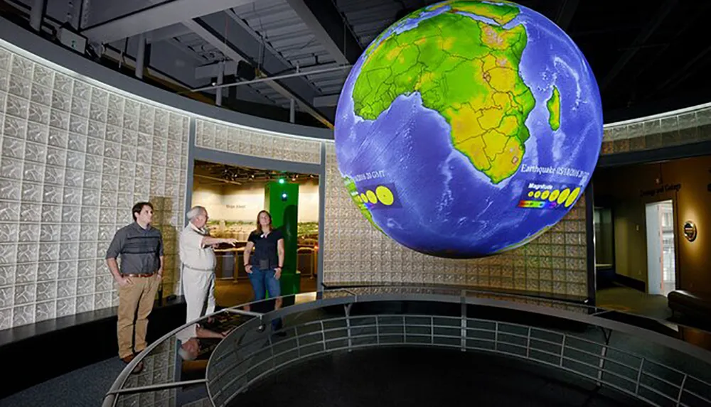 Three individuals are observing a large suspended globe exhibit inside a room that appears to be part of a museum or educational center
