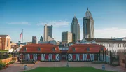 The image shows historic half-timbered buildings in the foreground with modern skyscrapers rising in the background under a clear sky.