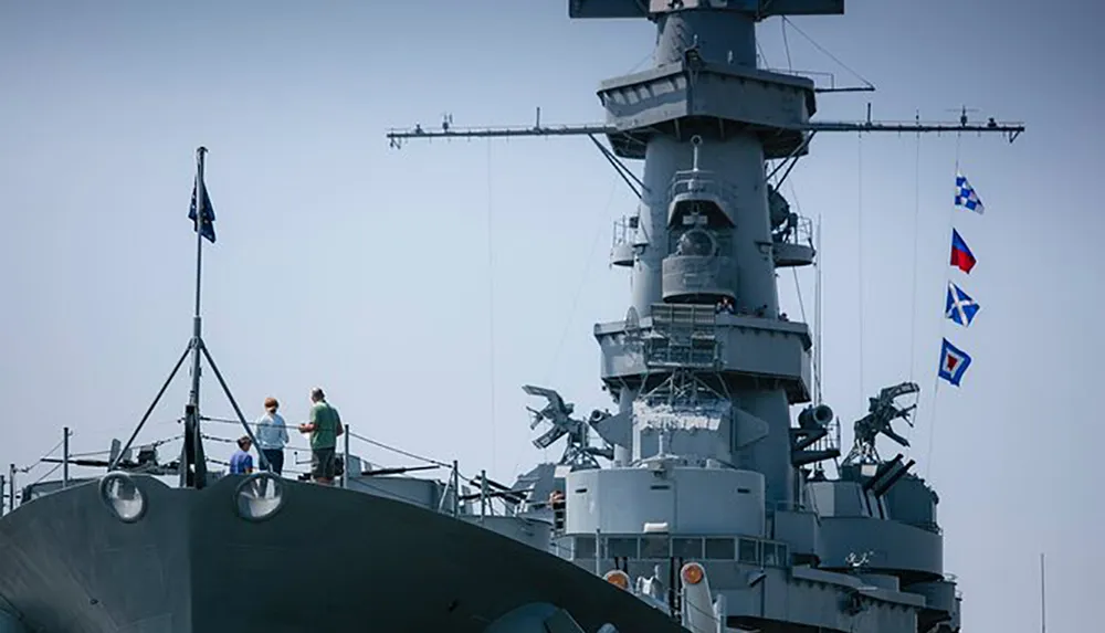A group of individuals is standing on the deck of a naval ship adorned with signal flags with some looking towards the camera