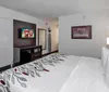 This is a modern hotel room featuring two queen beds with patterned bedspreads a desk with chairs a mounted television displaying a football player and red accent walls