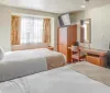 The image shows a tidy hotel room with two neatly made queen-size beds a large mirror and modern furnishings