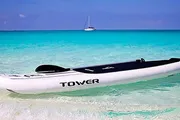 A paddleboard rests on the clear, shallow waters of a tropical beach with a sailboat in the distance.