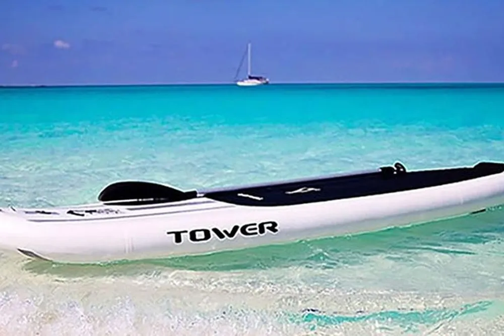A paddleboard rests on the clear shallow waters of a tropical beach with a sailboat in the distance