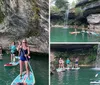 A group of people are paddleboarding near a waterfall and a rocky cliff