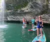 A group of people are paddleboarding near a waterfall and a rocky cliff