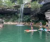 A group of people are paddleboarding near a waterfall and a rocky cliff