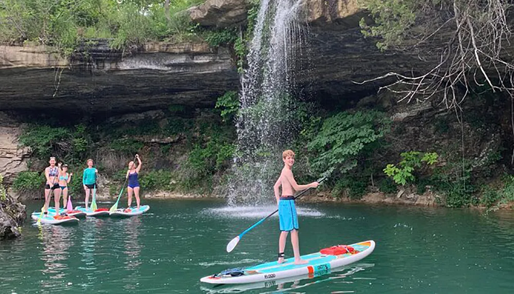 A group of people are enjoying paddleboarding on a serene water body in front of a scenic waterfall