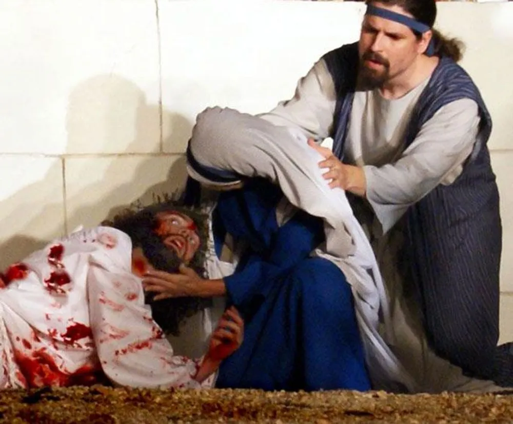 The image depicts a dramatic scene where two individuals dressed in historical garments appear to be tending to a third person who is covered in blood