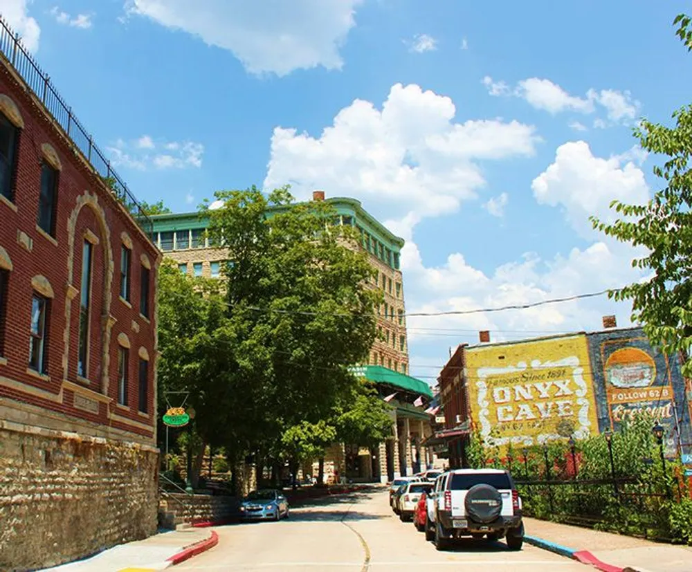 The image shows a sunny street view with historic brick buildings vintage advertisements painted on the sidewalls cars parked along the curb and a clear blue sky with fluffy clouds