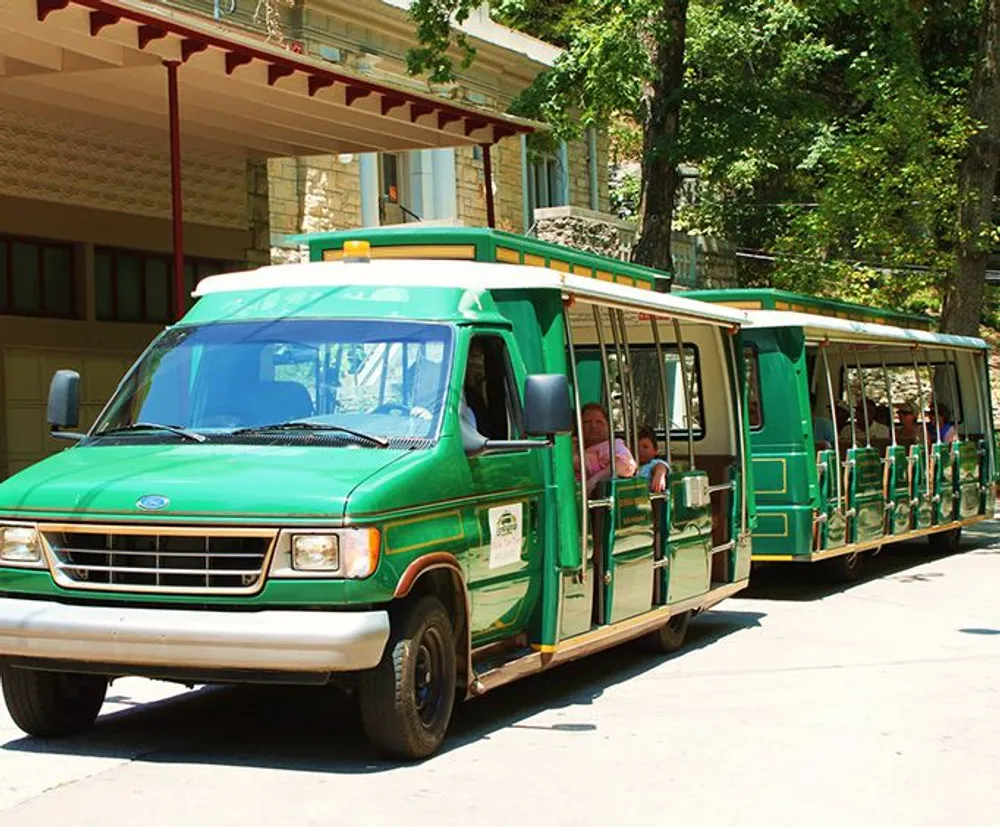 This image shows a green tram-like tour vehicle with multiple connected carriages filled with passengers