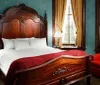 The image shows a classically decorated bedroom with an ornate wooden bed red bedding traditional furniture and heavy drapes framing a window