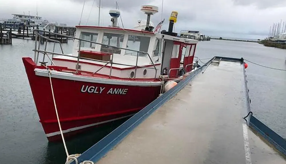 A red boat named UGLY ANNE is docked at a pier on an overcast day