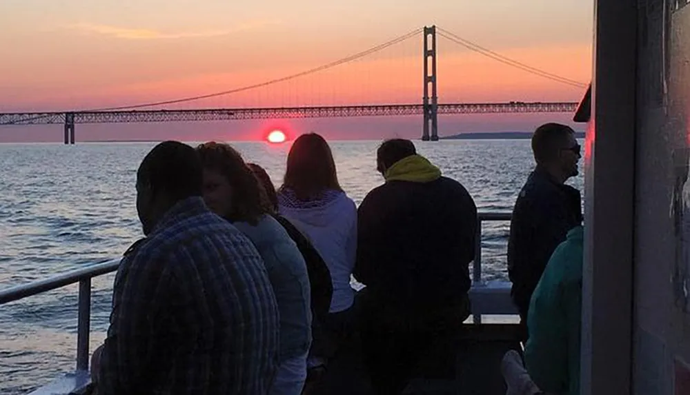 People are watching a sunset near a bridge possibly from a boat or a waterfront