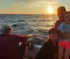 A group of people enjoys a scenic sunset aboard a boat with a child in sunglasses smiling at the forefront
