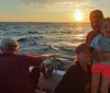 A group of people enjoys a scenic sunset aboard a boat with a child in sunglasses smiling at the forefront