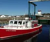 A vibrant red boat named UGLYANNE is moored at a wooden dock under a clear blue sky