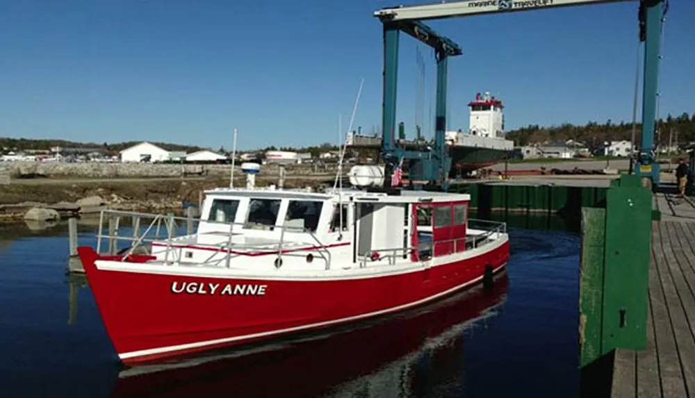 A vibrant red boat named UGLYANNE is moored at a wooden dock under a clear blue sky