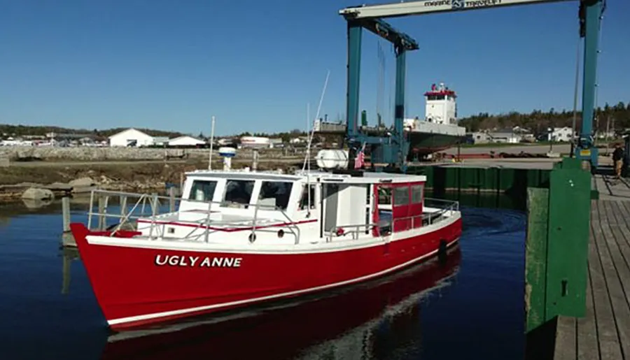 A vibrant red boat named UGLYANNE is moored at a wooden dock under a clear blue sky.